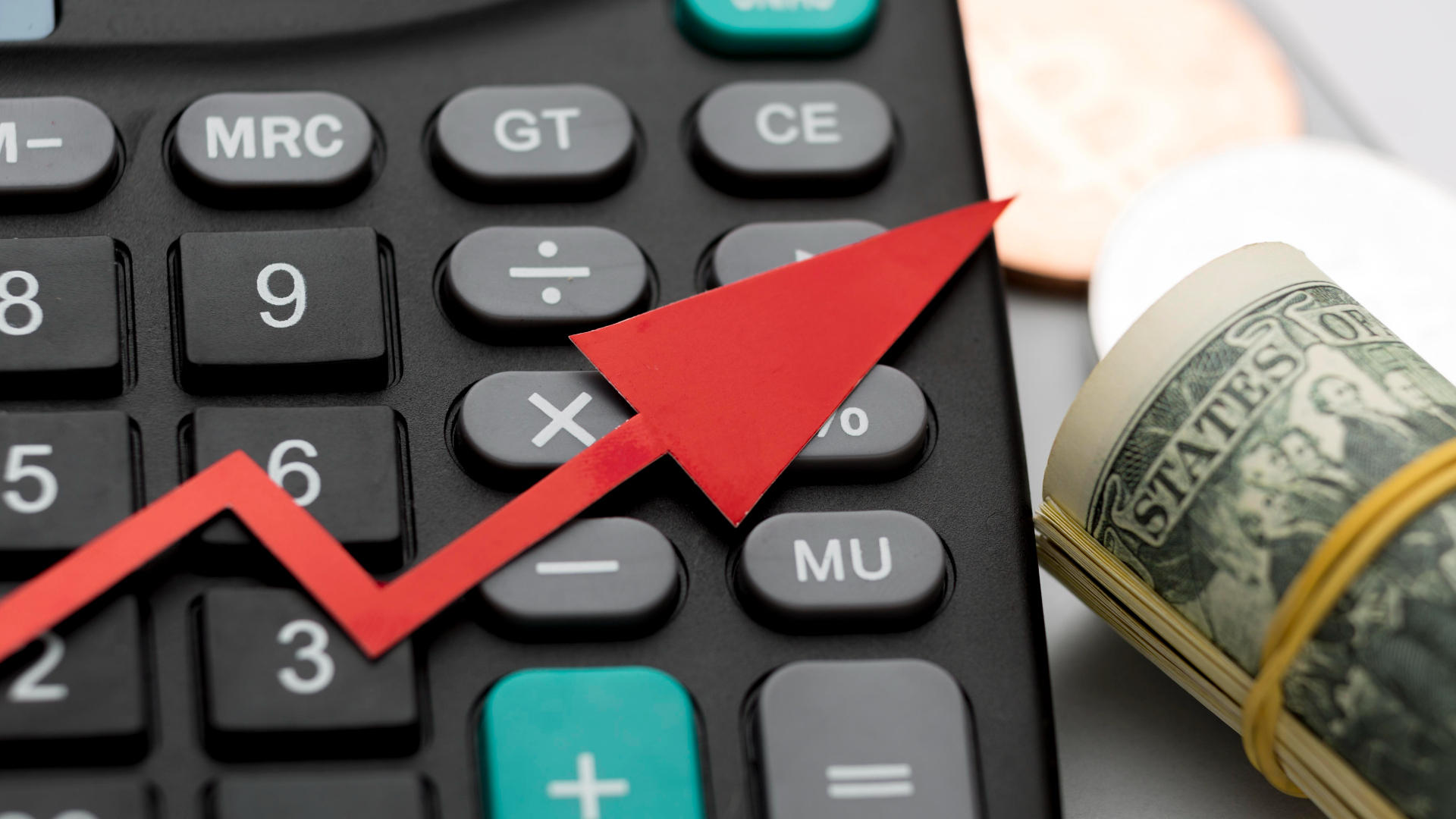 Uma seta vermelha para cima fica em uma calculadora preta, simbolizando crescimento ou ganho financeiro. Ao lado dela, um rolo de notas de dólar americano é preso com um elástico, ao lado de moedas borradas. A imagem sugere temas de gestão de dinheiro e o que poderia ser visto como uma explicação visual do aumento do lucro. - Efacont