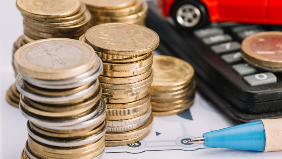 Pilhas de moedas são colocadas em um gráfico financeiro, perto de uma caneta de ponta azul. Um carrinho de brinquedo vermelho fica em uma calculadora ao fundo, sugerindo finanças empresariais e necessidades de orçamento, talvez explorando o que o Fondo de Maneio é em gerenciamento de despesas com automóveis. - Efacont