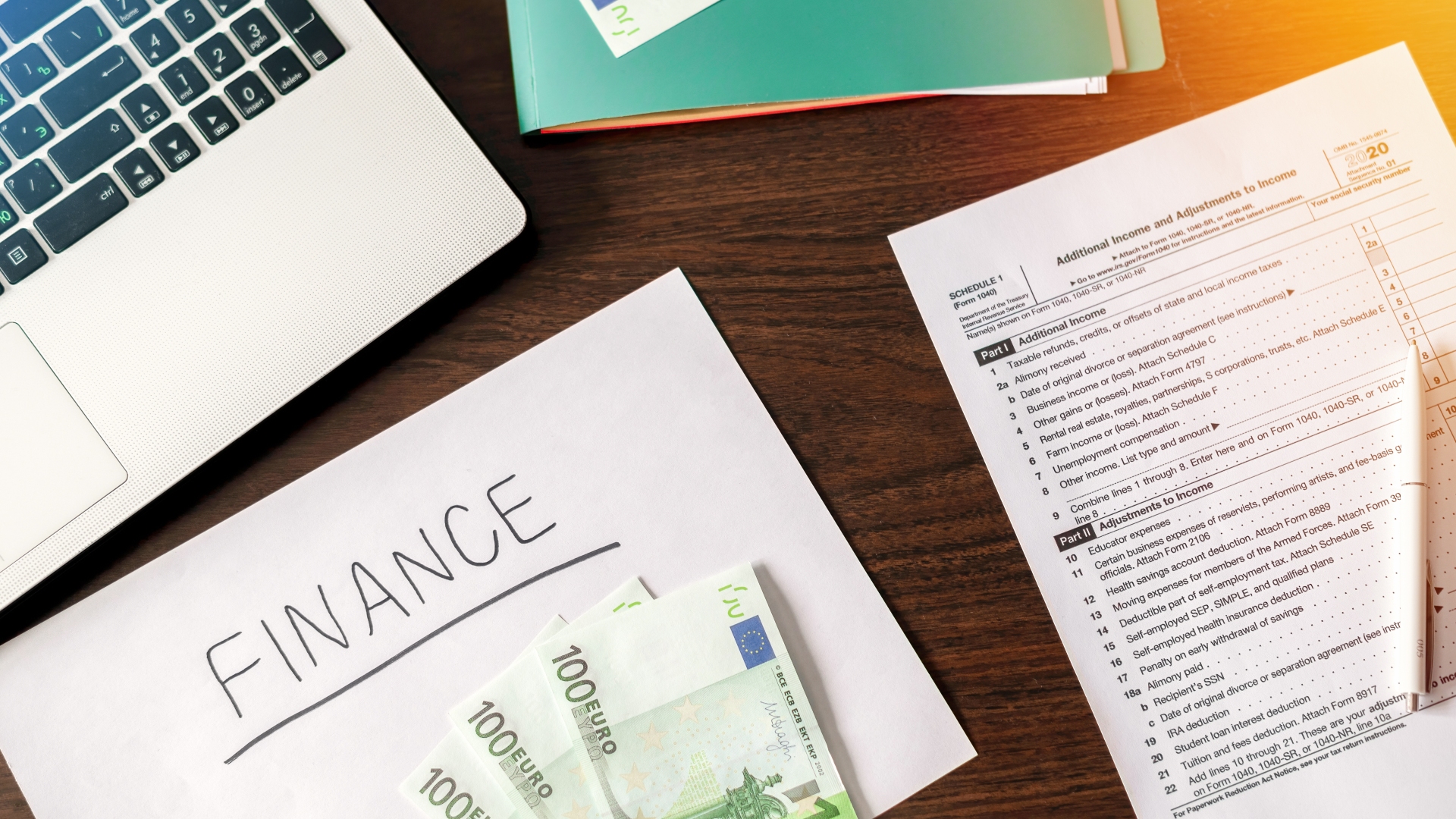 Uma mesa com um laptop, um documento rotulado "Finanças", notas de euro e um formulário de imposto explicando "dívida subordinada". O laptop está parcialmente visível, enquanto o formulário apresenta informações impressas detalhadas. Uma pasta ou caderno verde está parcialmente visível no canto, tudo em uma superfície de madeira escura. - Efacont