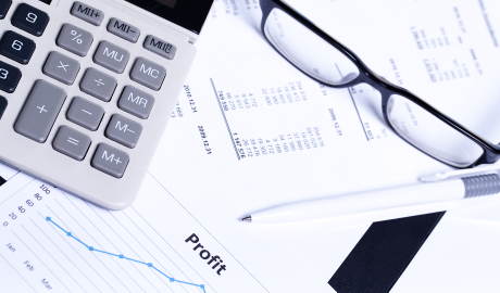 Uma calculadora, óculos e uma caneta são colocados em documentos financeiros detalhando dados numéricos e gráficos. Uma seção rotulada "Lucro" e um gráfico de linha azul sugerem uma análise de margem bruta para desempenho financeiro. O cenário é claro e organizado. - Efacont