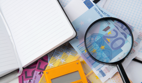 Uma mesa desorganizada exibe um caderno aberto, notas bancárias europeias e uma lupa focando em uma nota de 20 euros. Papel quadriculado é parcialmente visível no fundo, e uma calculadora amarela fica proeminentemente perto do primeiro plano, sugerindo análise financeira ou planejamento com atenção às palavras-chave de SEO. - Efacont