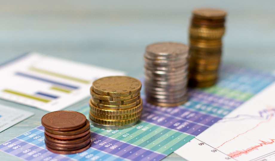 Pilhas de moedas variadas estão dispostas em ordem crescente em gráficos financeiros coloridos, sugerindo crescimento financeiro, investimentos ou diferentes tipos de obrigações. O fundo desfocado mantém o foco nas moedas e nos gráficos detalhados abaixo delas. - Efacont