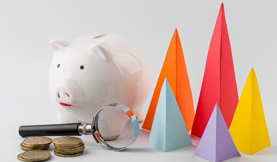 Um cofrinho branco fica ao lado de moedas empilhadas e uma lupa, simbolizando o escrutínio financeiro para entender margem líquida. À direita, quatro pirâmides de papel coloridas em laranja, vermelho, azul e roxo estão dispostas contra um fundo cinza claro simples. - Efacont