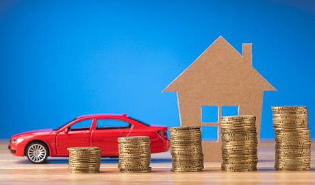Um pequeno modelo de carro vermelho é posicionado ao lado de pilhas de altura crescente feitas de moedas de ouro, ilustrando crescimento financeiro ou investimento — conceitos frequentemente explorados ao discutir o que é um leasing. Atrás deles, uma casa recortada de papelão contra um fundo azul simboliza imóveis ou propriedade de casa. - Efacont