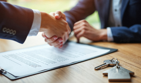 Duas pessoas em trajes de negócios apertam as mãos sobre uma mesa de madeira com um contrato em foco. Ao lado do documento, chaves sugerem um acordo de propriedade, possivelmente relacionado a contratos de arrendamento, como o que é leasing operacional. O fundo suavemente desfocado destaca o aperto de mão e o significado do contrato. - Efacont