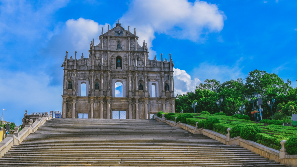 A imagem mostra a fachada de pedra das Ruínas de São Paulo, em Macau, contra um céu azul brilhante com nuvens - um marco icônico que simboliza a oportunidade de crescimento de Macau em meio à sua rica história e aos prósperos arredores. - Efacont